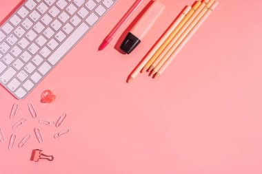 Pembe arkaplandaki klavyenin yanındaki kalemler ve işaretler.