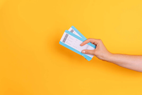 Рука держит билеты на желтом фоне.