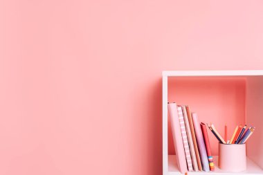 Okul gereçleri ve kitapları pembe arka planda beyaz bir rafta duruyor..