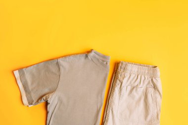 Açık gri çocuk kıyafetleri, pantolonlu tişörtler. Moda çocuk kıyafetleri yaz ve bahar için. Sarı arka planda tamamen gri görünüm. Düz yatış, üst görünüm.