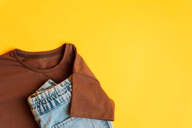 Sarı arka planda bahar, sonbahar ya da yaz için kahverengi tişört ve kot pantolon ve aksesuarlar. Moda çocuk kıyafeti. Düz yatış, üst görünüm.
