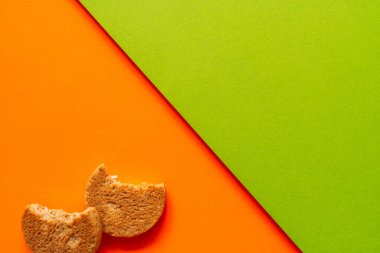 Parlak turuncu ve yeşil kağıttan arka planda iki ısırılmış kurabiye. Minimalist geometrik besin kompozisyonu canlı pop sanat tarzında. Yüksek kalite fotoğraf