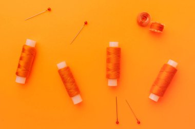 Turuncu dikişli makara iplikler turuncu renkli arka planda iğneler, moda ve el yapımı el yapımı aksesuarlar..