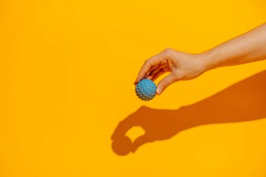 Turuncu arka planda kendine masaj yapmak için mavi dikenli masaj topunu tutuyor. Yüksek kalite fotoğraf