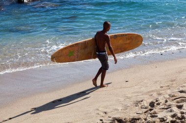 Saint Gilles les Bains, La Reunion - June 13 2017: Teenager holding his surfboard while walking at the edge of the Plage des Roches Noires (Beach of the black rocks).