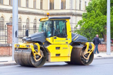 Varna, Bulgaria - May 16 2019: A Bomag compactor smoothing asphalt freshly spread on a downtown road.