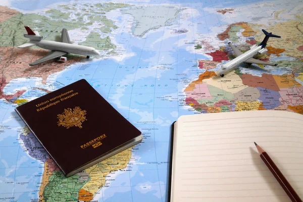 世界地图 上面有两架玩具飞机 一本法国护照和一支圆珠笔在一个开着的记事本的顶部 — 图库照片