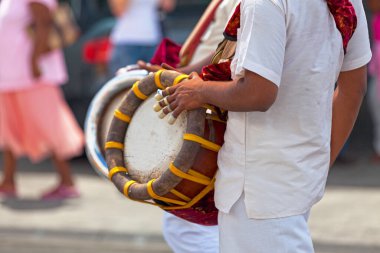 Close-up on a musician playing with a Thavil during a Tamil procession.