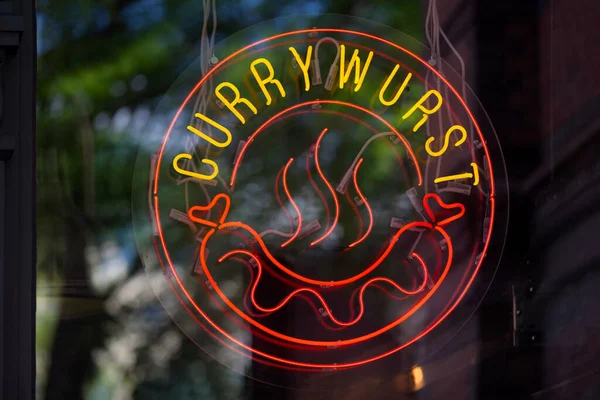 Circular neon light at a restaurant\'s window showing a Curry wurst.