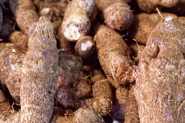Full frame close-up on a stack of purple yams on a market stall.