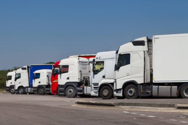 Row of cab over semi-trailer trucks parked in a highway parking lot.