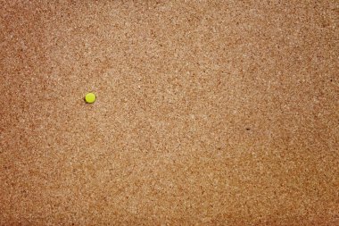 Full frame bulletin board made of cork with a single yellow thumbtack pinned to it.