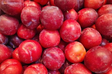 Close-up on a stack of red plums for sale on a market stall.