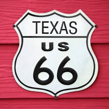 Close-up on an Texas US 66 route sign screwed on a wooden wall painted in red.