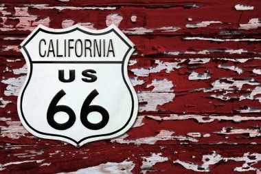 Close-up on an California US 66 route sign screwed on a wooden wall painted in red.
