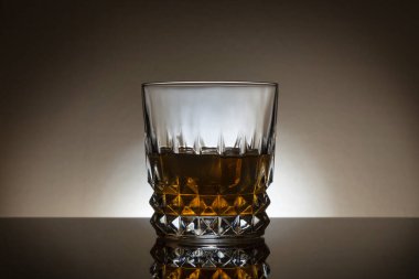 Backlit Whiskey glass on a dark background with reflection in front of the glass.