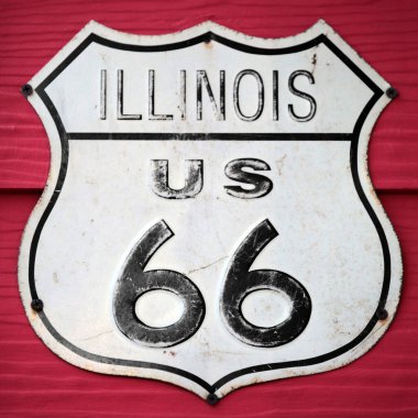 Close-up on an Illinois US 66 route sign screwed on a wooden wall painted in red.