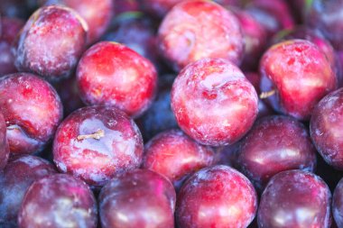 Close-up on a stack of red plums for sale on a market stall.
