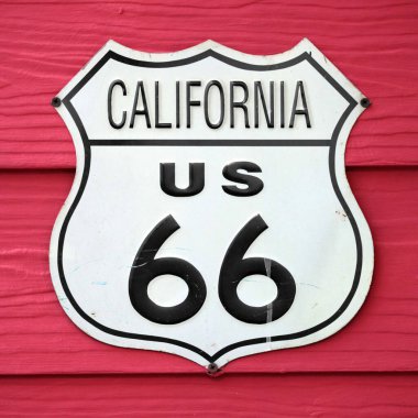 Close-up on an California US 66 route sign screwed on a wooden wall painted in red.