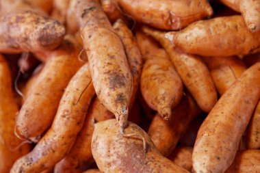 Full frame close-up on a stack of patate carottes (orange skinned sweet potatoes) on a market stall.