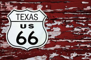 Close-up on an Texas US 66 route sign screwed on a wooden wall painted in red.