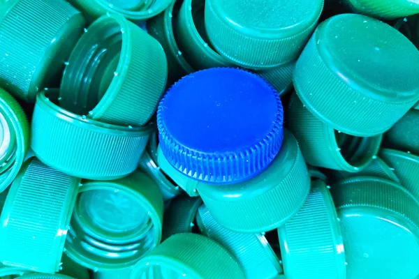 Blue plastic cap in the middle of green plastic caps.