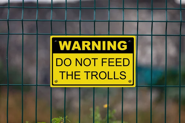 Black and yellow warning sign attached on a fence. The sign stating : Warning, Do not feed the trolls.