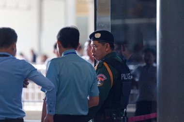 Phnom Penh, Kamboçya - 01 Eylül 2018: Kurşungeçirmez yelek giyen polis, Phnom Penh Uluslararası Havalimanı 'nın ana girişinin yanında iki çalışanıyla konuşuyor.