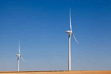 Bir tepenin arkasından çıkan iki rüzgar türbini..