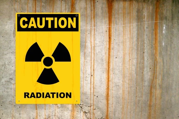 黄色的警示牌钉在水泥墙上警告人们注意威胁 在面板的中间 有一个辐射符号 上面写着 — 图库照片
