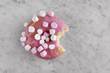 Üzerinde küçük şekerlemeler olan pembe kremalı çörek ve bir lokma eksik..