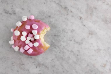 Üzerinde küçük şekerlemeler olan pembe kremalı çörek ve bir lokma eksik..