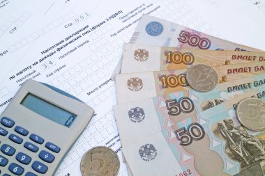 Rus gelir vergisi formunun üstüne bir hesap makinesi ve birkaç ruble bozukluk ve banknotlar..
