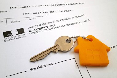 Boş konutların konut vergisi için Fransızca formunun üstüne anahtarlığını iliştirmiş bir kapı anahtarı (Avis d 'impot - Taxe d' habitation sur les bos konutlar).