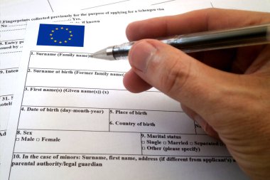 Schengen vize başvuru formunu doldurmaya hazır birinin parmağından tutulan kalem..