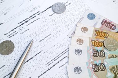 Rus gelir vergisi formunun üstüne bir kalem, birkaç ruble bozukluk ve banknotlar..