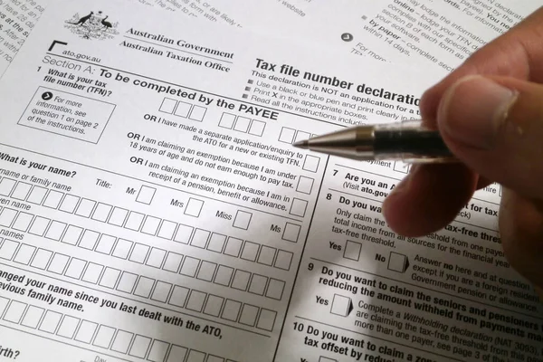 A pen hold by the fingers of somebody ready to fill an Australian Tax file number declaration form.