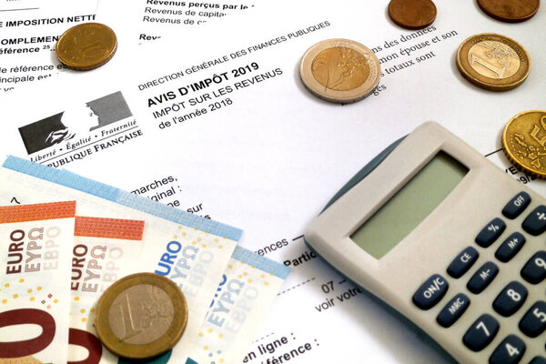 A calculator and some euro coins and banknotes on the top of a French income tax form (Avis d 'impot sur les Revus).