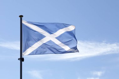 Scottish Saltire flag (St. Andrew's Cross) waving atop of its pole against a blue sky.