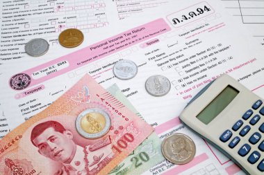 Bangkok, Tayland - Ekim 05 2018: Bir hesap makinesi ve Tayland gelir vergisi formunun tepesindeki baht madeni paralar ve banknotlar.