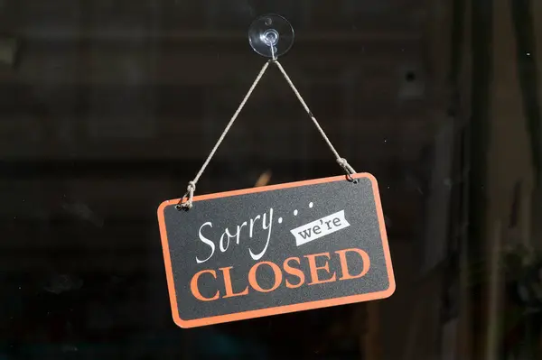 Black  and orange sign hanging at the glass door of a shop saying \