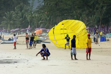 Patong plajı, Tayland - 11 Temmuz 2007: Genç bir beyaz turist Phuket 'teki Patong plajında yamaç paraşütü yapmaya hazırlanırken genç Taylandlı erkekler Petanque oynuyorlar.