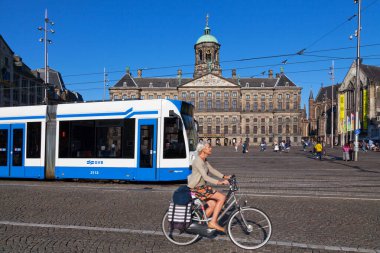Amsterdam, Hollanda - 27 Ağustos 2017: Bisikletli ve tramvaylı bir bayan arkasında Dam Meydanı 'ndan önce geçen Madame Tussaud, Amsterdam Kraliyet Sarayı ve Nieuwe Kerk.