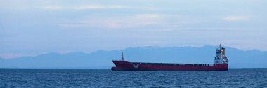 Thessaloniki, Greece - May 03 2019: Cargo ship in the Thermaic Gulf in anchorage in front of the snowcapped mountains at sunset. clipart