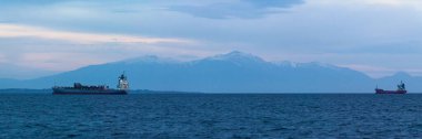 Selanik, Yunanistan - 03 Mayıs 2019: Günbatımında Olimpos Dağı 'nın karlı zirvesi önünde Selanik körfezinde demirli kargo gemileri.