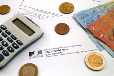 A calculator and some euro coins and banknotes on the top of a French property tax form (Avis de Taxes foncieres). clipart