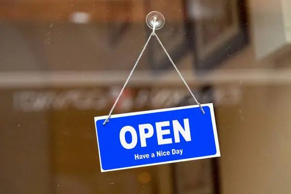 Blue sign open sign anging at the glass door of a shop saying: \