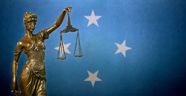 stock image Close-up of a small bronze statuette of Lady Justice before a flag of the Federated States of Micronesia.