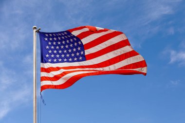 Mavi gökyüzüne karşı havada dalgalanan Amerikan bayrağı.