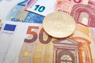 Altın bir Bitcoin 'in üzerine yakın plan bir yığın Euro banknotunun üstüne.